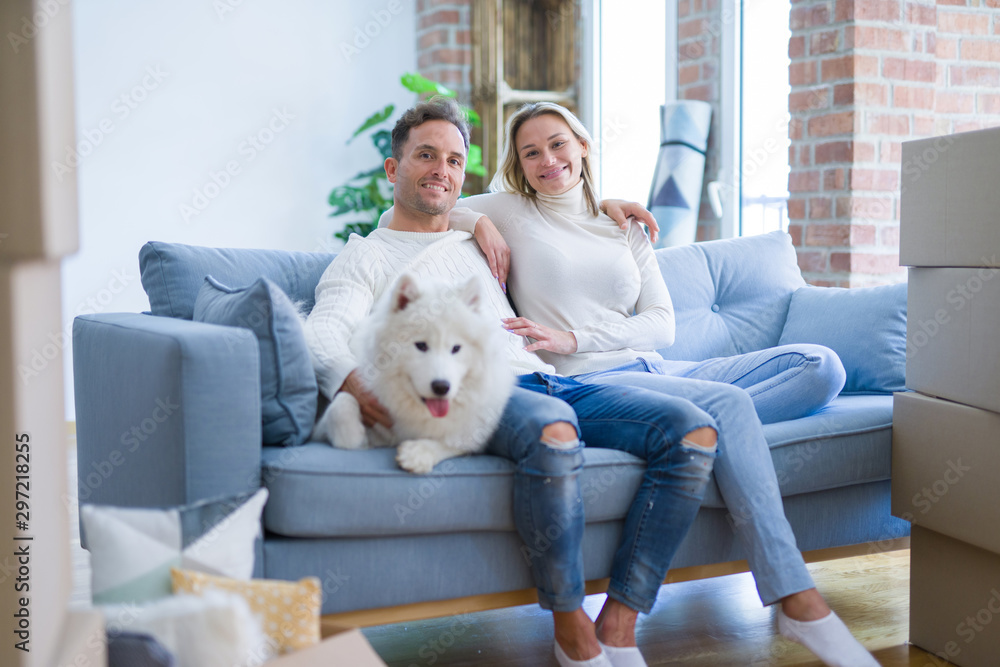 Young beautiful couple with dog sitting on the sofa at new home around cardboard boxes Young beautiful couple with dog sitting on the sofa at new home around cardboard boxes