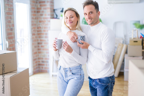 Young beautiful couple standing drinking cup of coffee at new home around cardboard boxes