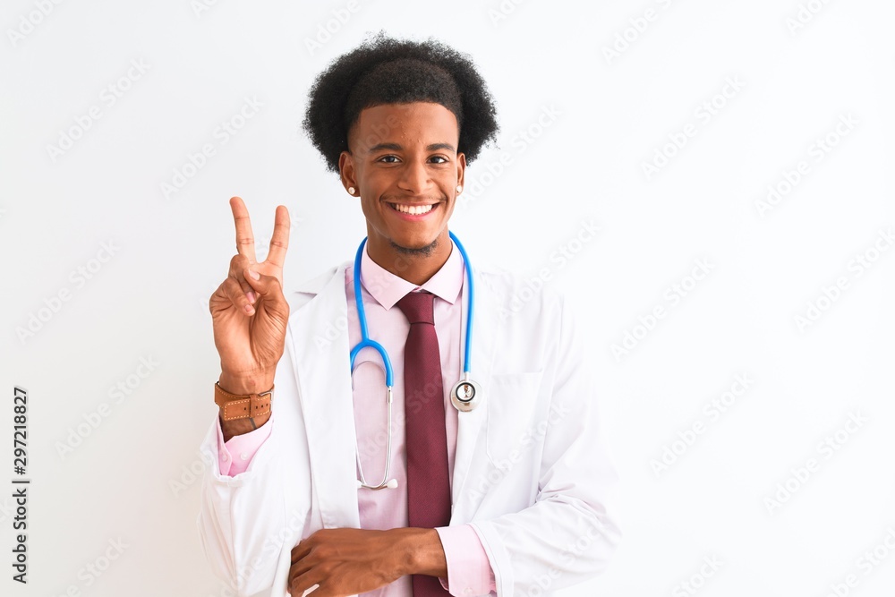Young african american doctor man wearing sthetoscope over isolated white background smiling with happy face winking at the camera doing victory sign. Number two. Young african american doctor man wearing sthetoscope over isolated white background smiling with happy face winking at the camera doing victory sign. Number two.