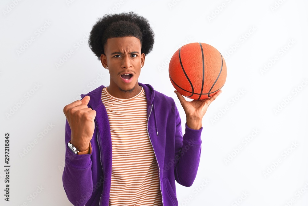 Young african american sportsman holding basketball ball over isolated white background annoyed and frustrated shouting with anger, crazy and yelling with raised hand, anger concept