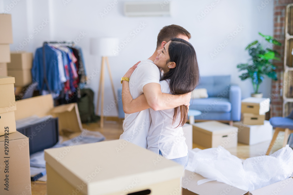 Young beautiful couple hugging at new home around cardboard boxes Young beautiful couple hugging at new home around cardboard boxes