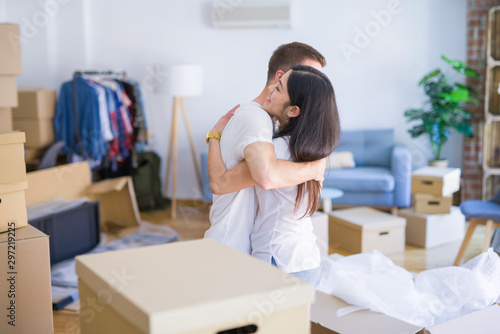 Young beautiful couple hugging at new home around cardboard boxes