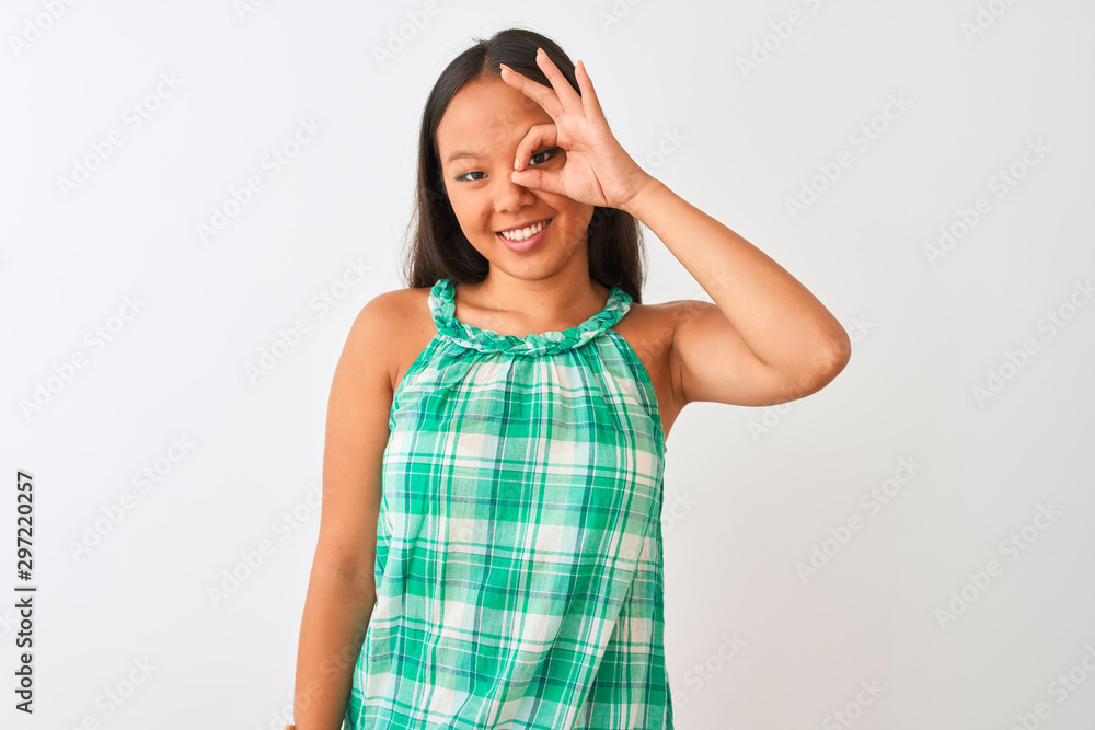 Young chinese woman wearing green dress standing over isolated white background doing ok gesture with hand smiling, eye looking through fingers with happy face. Young chinese woman wearing green dress standing over isolated white background doing ok gesture with hand smiling, eye looking through fingers with happy face.