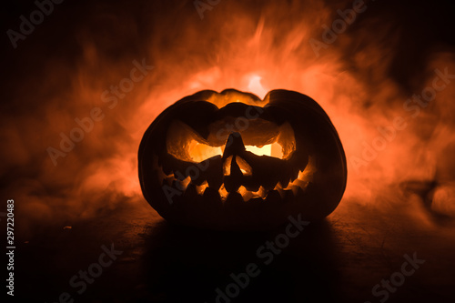 Close up view of scary Halloween pumpkin with eyes glowing inside at black background. Selective focus