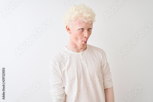 Young albino blond man wearing casual t-shirt standing over isolated white background making fish face with lips, crazy and comical gesture. Funny expression.