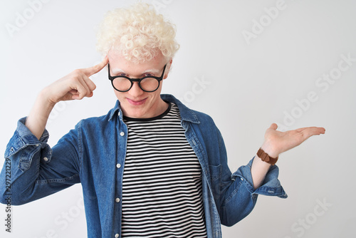 Young albino blond man wearing denim shirt and glasses over isolated white background confused and annoyed with open palm showing copy space and pointing finger to forehead. Think about it.