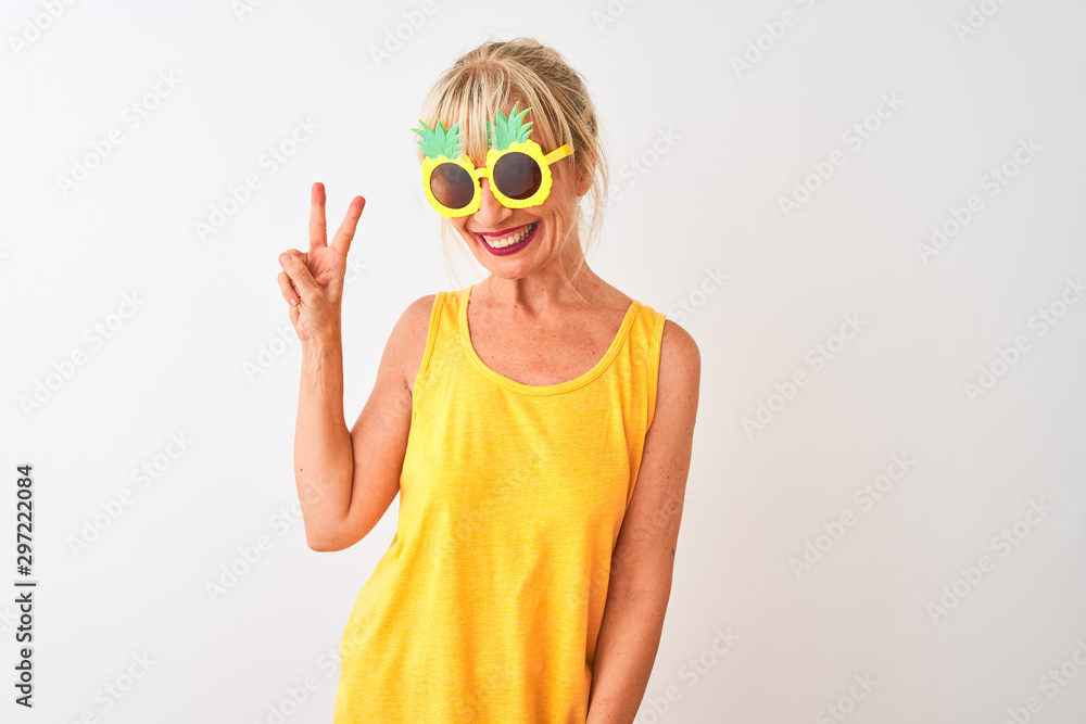 Middle age woman on vacation wearing pineapple sunglasses over isolated white background smiling with happy face winking at the camera doing victory sign. Number two.