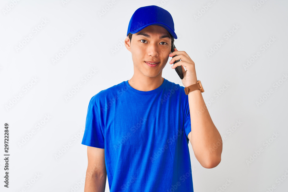 Chinese deliveryman wearing cap talking on the smartphone over isolated white background with a happy face standing and smiling with a confident smile showing teeth Chinese deliveryman wearing cap talking on the smartphone over isolated white background with a happy face standing and smiling with a confident smile showing teeth