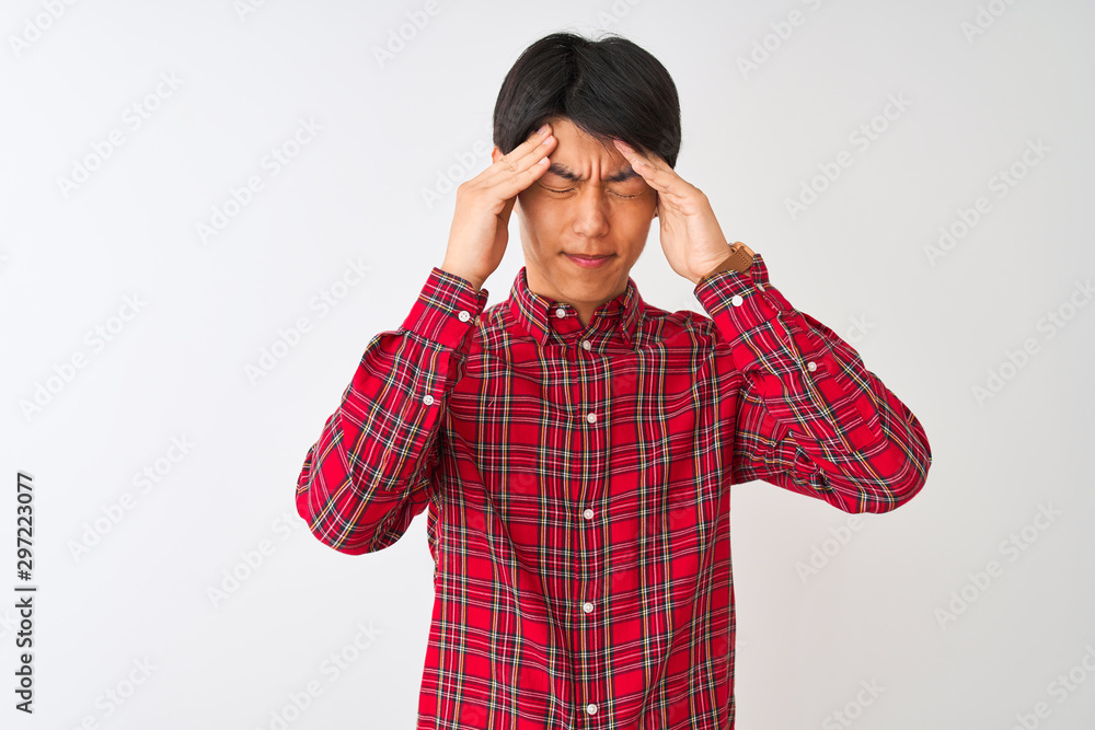 Young chinese man wearing casual red shirt standing over isolated white background suffering from headache desperate and stressed because pain and migraine. Hands on head. Young chinese man wearing casual red shirt standing over isolated white background suffering from headache desperate and stressed because pain and migraine. Hands on head.