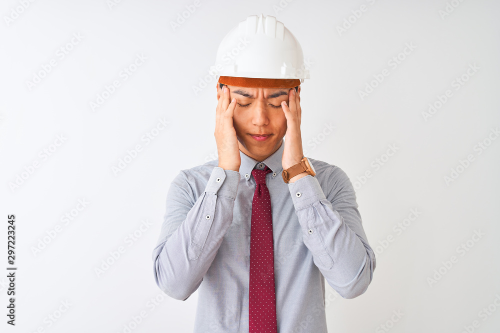 Chinese architect man wearing tie and helmet standing over isolated white background with hand on head for pain in head because stress. Suffering migraine. Chinese architect man wearing tie and helmet standing over isolated white background with hand on head for pain in head because stress. Suffering migraine.