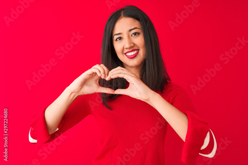 Young beautiful chinese woman wearing casual dress standing over isolated red background smiling in love showing heart symbol and shape with hands. Romantic concept.