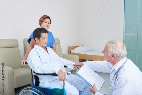 Doctor visiting senior patient in nursing home and asking him about health and recovery process