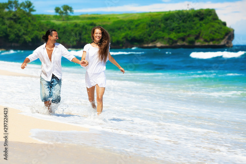 Happy family on honeymoon holiday - just married young couple having fun, run by water edge along sea beach surf. Active lifestyle, people recreational activity on summer vacation on tropical island. photo
