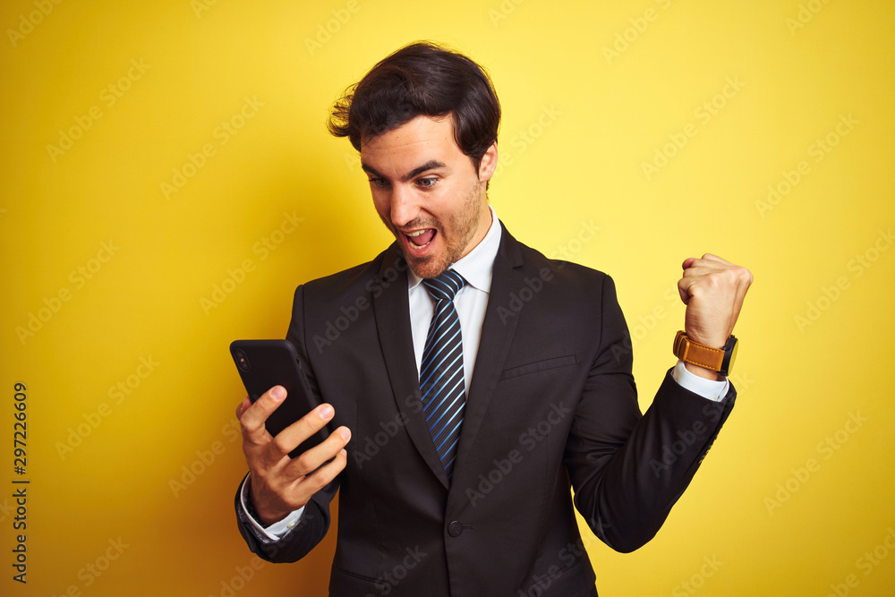 Young handsome businessman using smartphone standing over isolated yellow background screaming proud and celebrating victory and success very excited, cheering emotion Young handsome businessman using smartphone standing over isolated yellow background screaming proud and celebrating victory and success very excited, cheering emotion