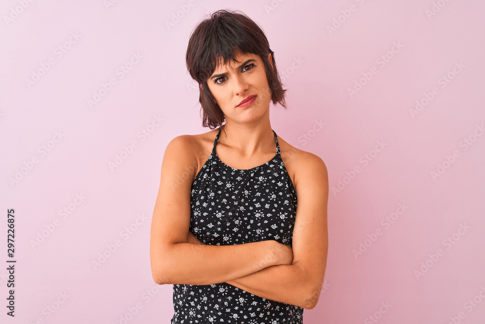 Young beautiful woman wearing black floral dress standing over isolated pink background skeptic and nervous, disapproving expression on face with crossed arms. Negative person. Young beautiful woman wearing black floral dress standing over isolated pink background skeptic and nervous, disapproving expression on face with crossed arms. Negative person.