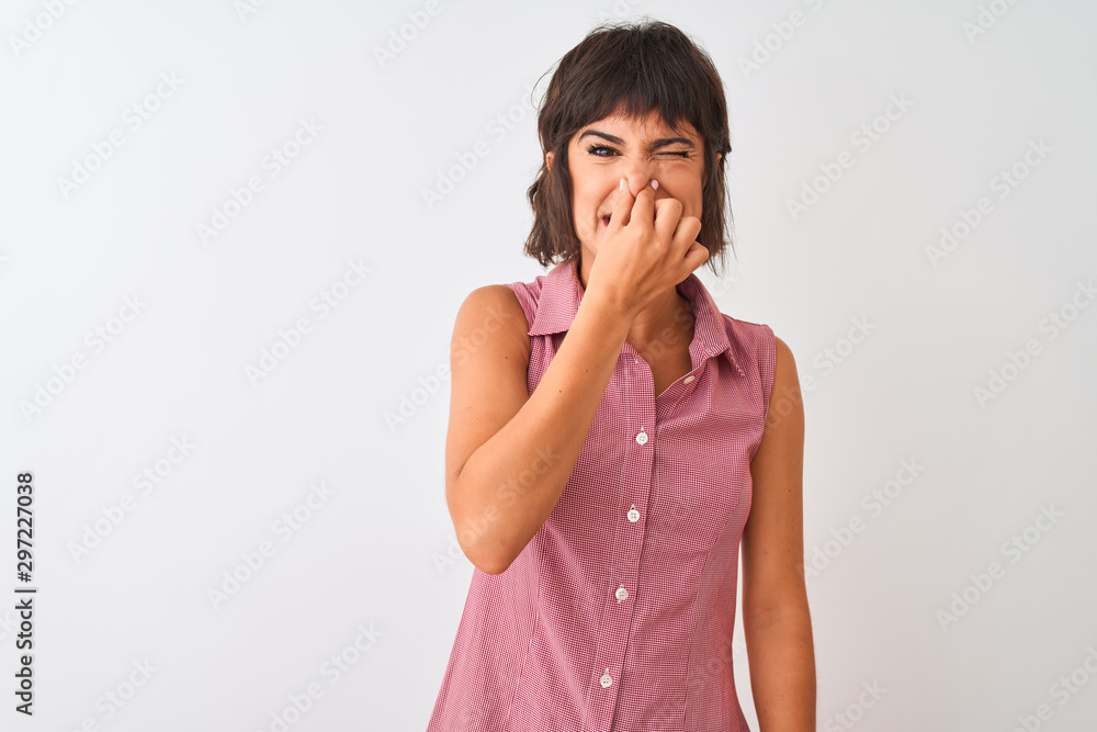 Young beautiful woman wearing red summer shirt standing over isolated white background smelling something stinky and disgusting, intolerable smell, holding breath with fingers on nose. Bad smell Young beautiful woman wearing red summer shirt standing over isolated white background smelling something stinky and disgusting, intolerable smell, holding breath with fingers on nose. Bad smell