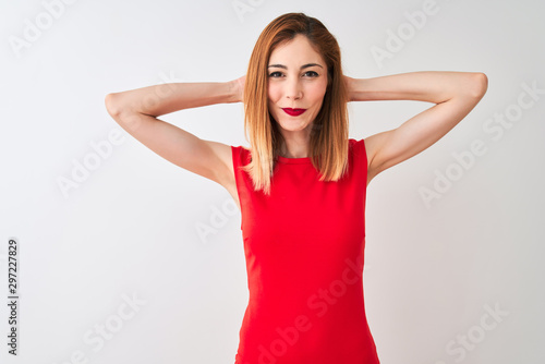Redhead businesswoman wearing elegant red dress standing over isolated white background relaxing and stretching  arms and hands behind head and neck smiling happy