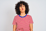 Young arab woman with curly hair wearing striped t-shirt over isolated white background making fish face with lips, crazy and comical gesture. Funny expression.