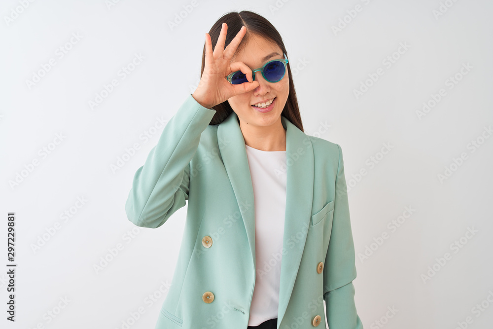 Chinese businesswoman wearing jacket and sunglasses over isolated white background with happy face smiling doing ok sign with hand on eye looking through fingers