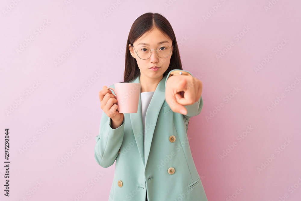 Young chinese businesswoman wearing glasses drinking coffee over isolated white background pointing with finger to the camera and to you, hand sign, positive and confident gesture from the front Young chinese businesswoman wearing glasses drinking coffee over isolated white background pointing with finger to the camera and to you, hand sign, positive and confident gesture from the front