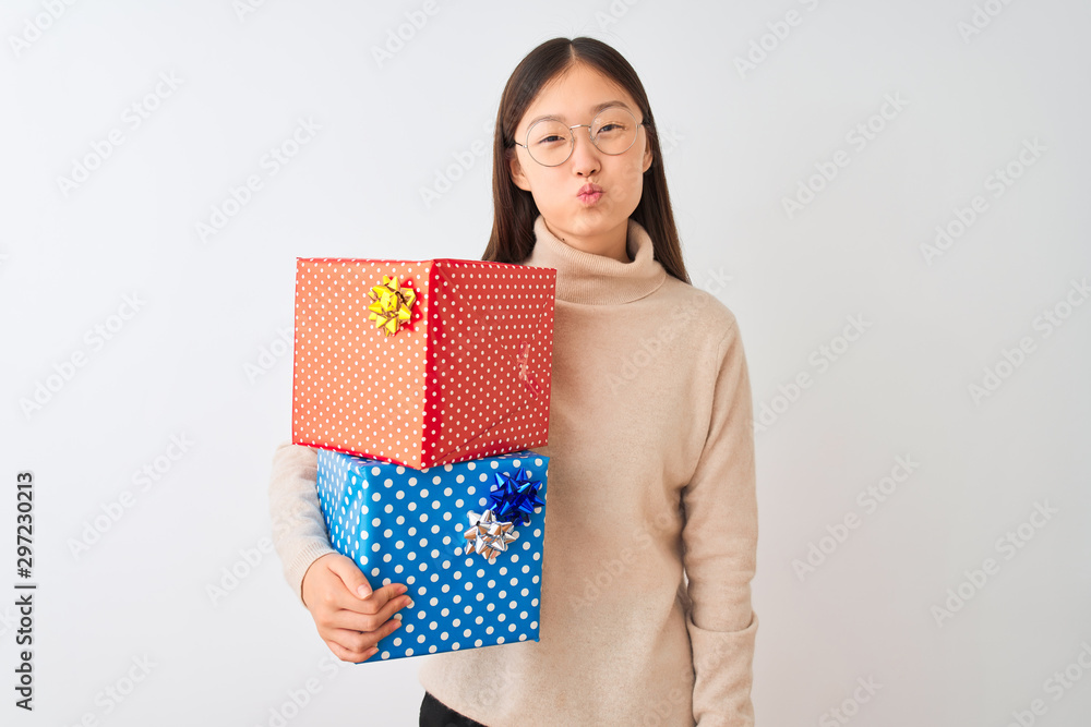 Young chinese woman holding birthday gifts over isolated white background puffing cheeks with funny face. Mouth inflated with air, crazy expression. Young chinese woman holding birthday gifts over isolated white background puffing cheeks with funny face. Mouth inflated with air, crazy expression.