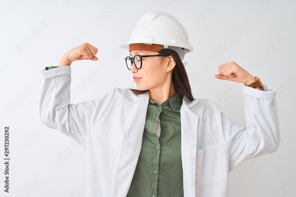 Young chinese engineer woman wearing coat helmet glasses over isolated white background showing arms muscles smiling proud. Fitness concept. Young chinese engineer woman wearing coat helmet glasses over isolated white background showing arms muscles smiling proud. Fitness concept.