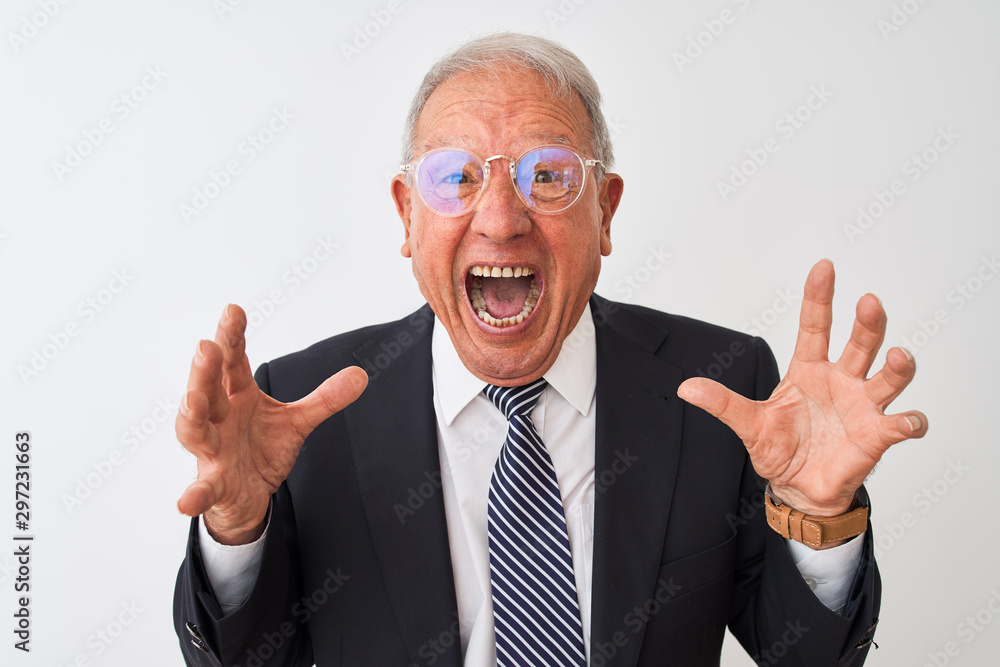 Senior grey-haired businessman wearing suit and glasses over isolated white background crazy and mad shouting and yelling with aggressive expression and arms raised. Frustration concept.