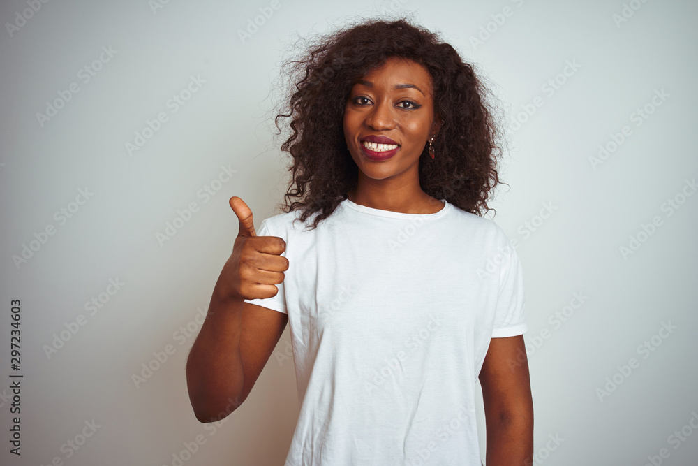 Young african american woman wearing t-shirt standing over isolated white background doing happy thumbs up gesture with hand. Approving expression looking at the camera showing success. Young african american woman wearing t-shirt standing over isolated white background doing happy thumbs up gesture with hand. Approving expression looking at the camera showing success.