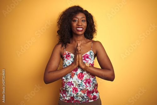 African american woman wearing floral summer t-shirt over isolated yellow background praying with hands together asking for forgiveness smiling confident.