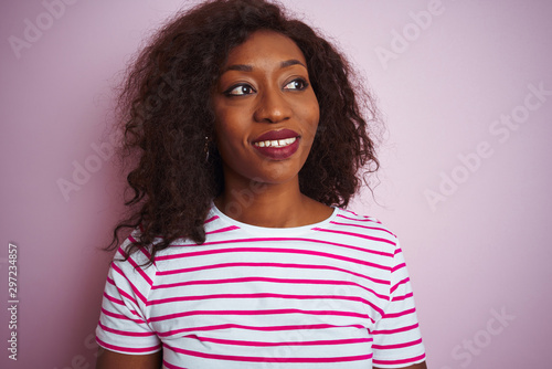 Young african american woman wearing striped t-shirt standing over isolated pink background looking away to side with smile on face, natural expression. Laughing confident. © Krakenimages.com
