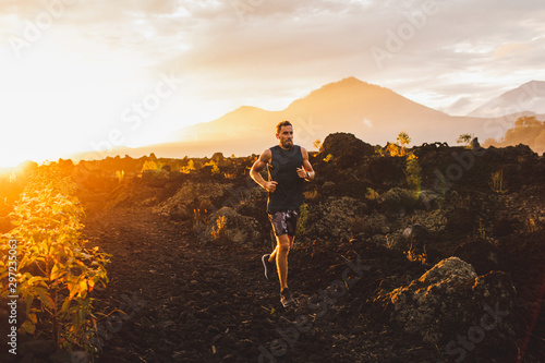 Young male athlete trail running in mountains at sunrise. Amazing black lava volcanic landscape of Bali on background. Adventure sport concept.