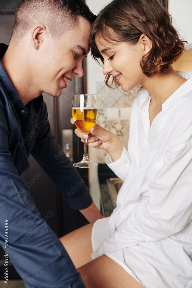Smiling boyfriend and girlfriend touching foreheads and looking at glass of wine Smiling boyfriend and girlfriend touching foreheads and looking at glass of wine