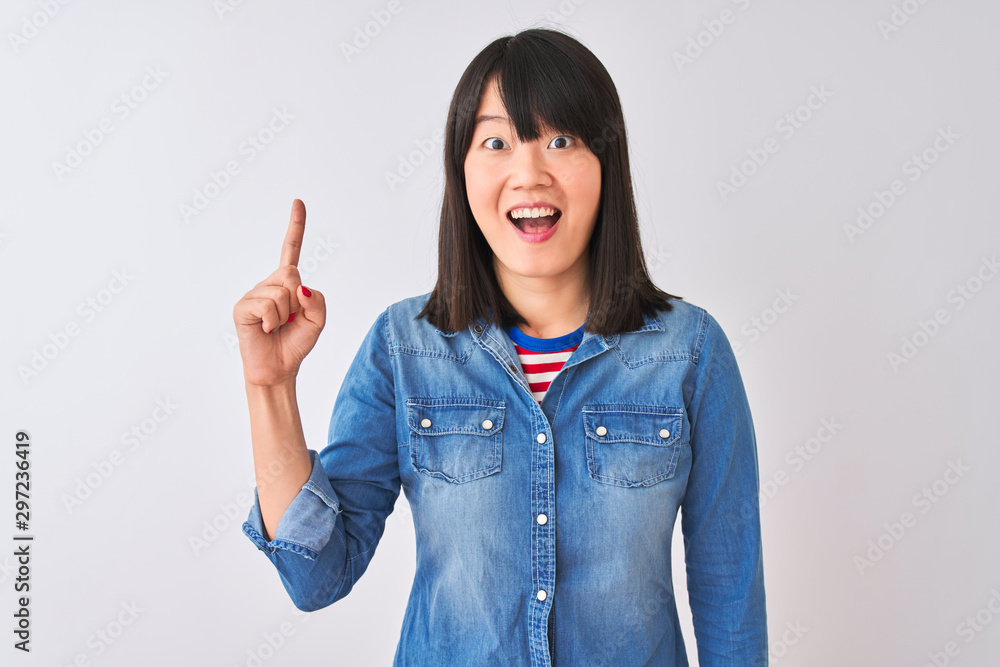 Young beautiful chinese woman wearing denim shirt over isolated white background pointing finger up with successful idea. Exited and happy. Number one.