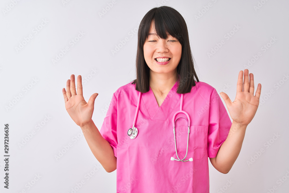 Young beautiful Chinese nurse woman wearing stethoscope over isolated white background showing and pointing up with fingers number ten while smiling confident and happy. Young beautiful Chinese nurse woman wearing stethoscope over isolated white background showing and pointing up with fingers number ten while smiling confident and happy.