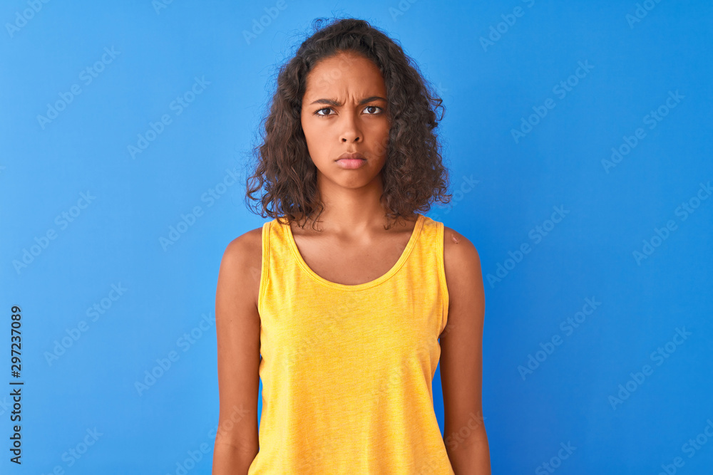 Young brazilian woman wearing yellow t-shirt standing over isolated blue background skeptic and nervous, frowning upset because of problem. Negative person. Young brazilian woman wearing yellow t-shirt standing over isolated blue background skeptic and nervous, frowning upset because of problem. Negative person.
