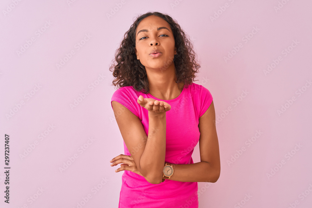 Young brazilian woman wearing t-shirt standing over isolated pink background looking at the camera blowing a kiss with hand on air being lovely and sexy. Love expression. Young brazilian woman wearing t-shirt standing over isolated pink background looking at the camera blowing a kiss with hand on air being lovely and sexy. Love expression.