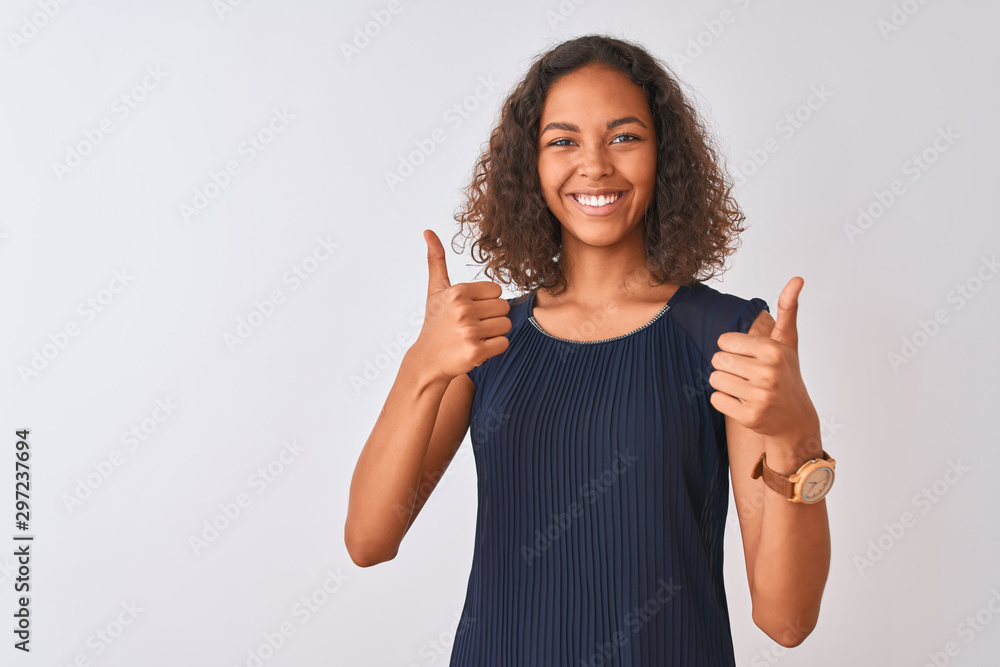 Young brazilian woman wearing blue dress standing over isolated white background success sign doing positive gesture with hand, thumbs up smiling and happy. Cheerful expression and winner gesture. Young brazilian woman wearing blue dress standing over isolated white background success sign doing positive gesture with hand, thumbs up smiling and happy. Cheerful expression and winner gesture.