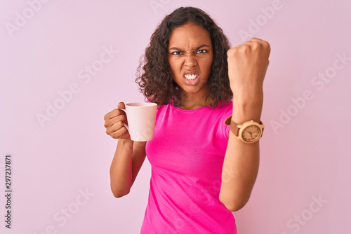 Young brazilian woman drinking cup of coffee standing over isolated pink background annoyed and frustrated shouting with anger, crazy and yelling with raised hand, anger concept