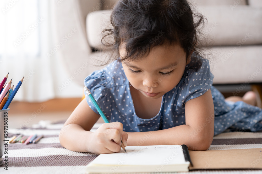 Asian little girl is drawing while lying on the carpet in the living room at her home Asian little girl is drawing while lying on the carpet in the living room at her home