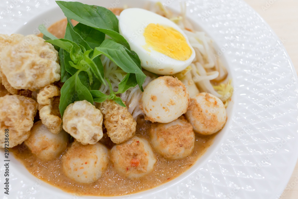 Thai Food Rice Noodles in Fish Curry With boiled egg, fish balls, pork snack, basil, bean sprouts on top, placed on a wooden table. Thai Food Rice Noodles in Fish Curry With boiled egg, fish balls, pork snack, basil, bean sprouts on top, placed on a wooden table.