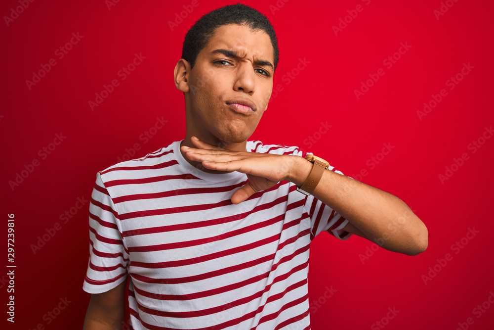 Young handsome arab man wearing striped t-shirt over isolated red background cutting throat with hand as knife, threaten aggression with furious violence Young handsome arab man wearing striped t-shirt over isolated red background cutting throat with hand as knife, threaten aggression with furious violence