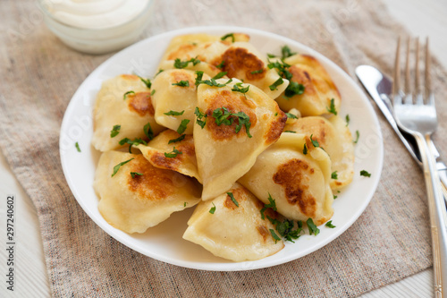 Homemade traditional polish fried potato pierogies on a white plate with sour cream, low angle view. Close-up.