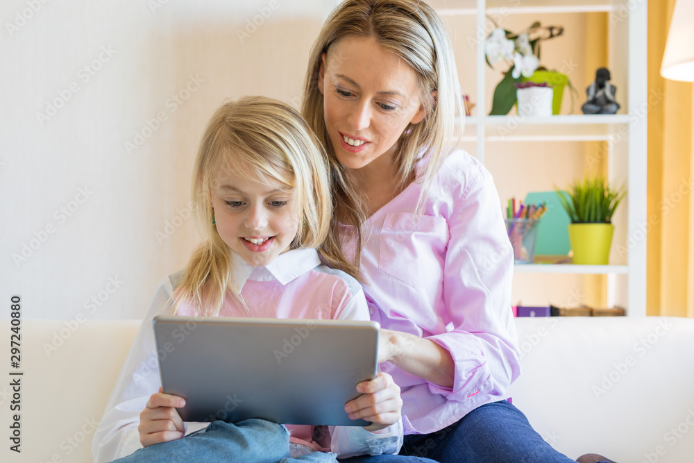 Blonde cheerful girl with her mother using tablet computer together Blonde cheerful girl with her mother using tablet computer together