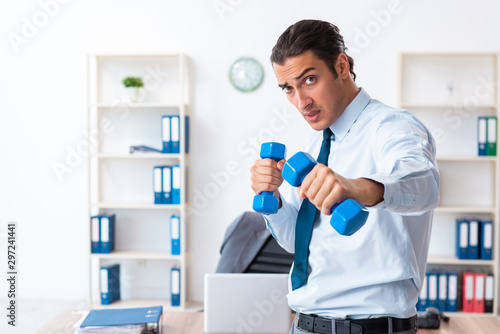 Young handsome employee doing sport exercises at workplace