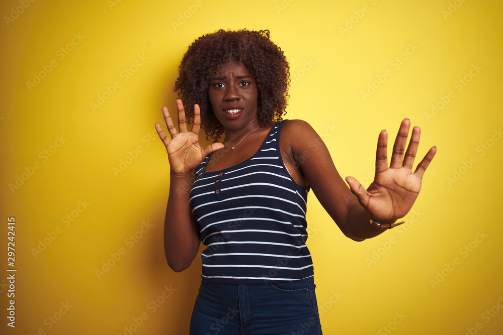 Young african afro woman wearing striped t-shirt over isolated yellow background afraid and terrified with fear expression stop gesture with hands, shouting in shock. Panic concept. Young african afro woman wearing striped t-shirt over isolated yellow background afraid and terrified with fear expression stop gesture with hands, shouting in shock. Panic concept.