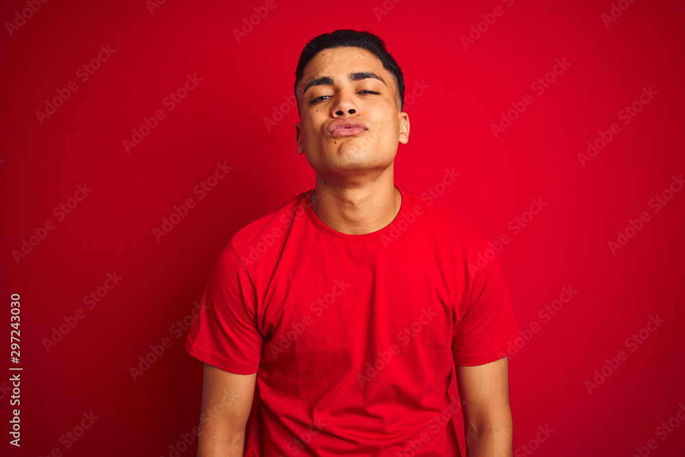 Young brazilian man wearing t-shirt standing over isolated red background looking at the camera blowing a kiss on air being lovely and sexy. Love expression. Young brazilian man wearing t-shirt standing over isolated red background looking at the camera blowing a kiss on air being lovely and sexy. Love expression.