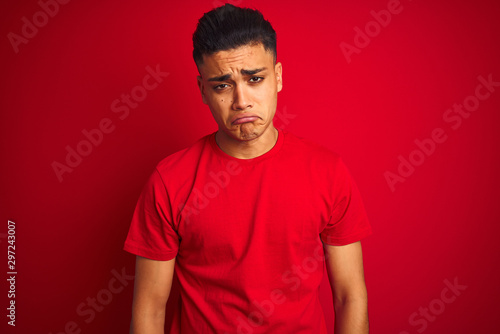 Young brazilian man wearing t-shirt standing over isolated red background depressed and worry for distress, crying angry and afraid. Sad expression.