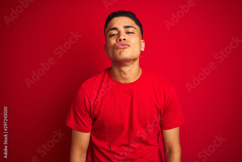 Young brazilian man wearing t-shirt standing over isolated red background looking at the camera blowing a kiss on air being lovely and sexy. Love expression.
