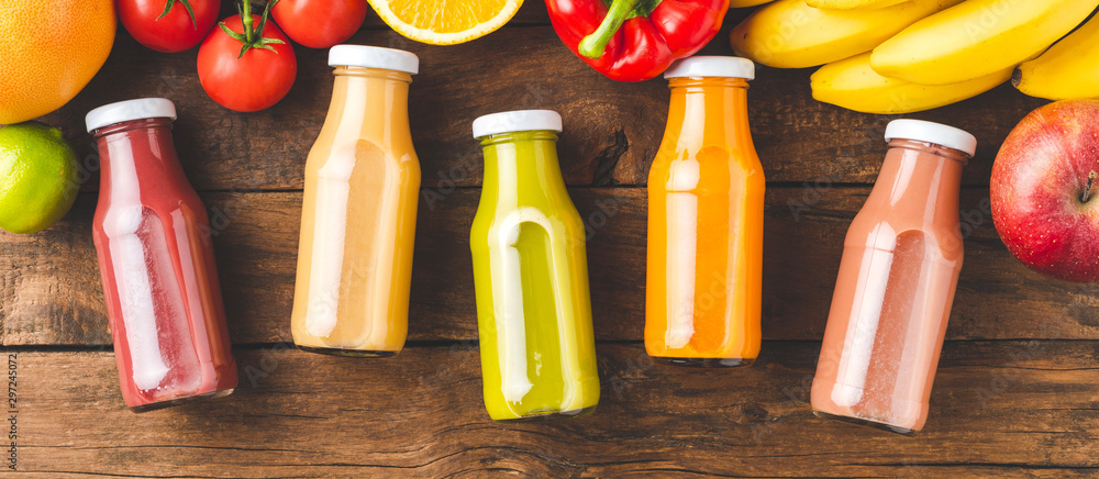 Multicoloured juices in bottles on old wooden background with fruits and vegetables. Top view. Banner - obrazy, fototapety, plakaty 