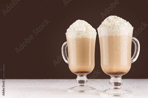 Coffee with whipped cream and foam in two goblets in brown modern restaurant interior  copy space.